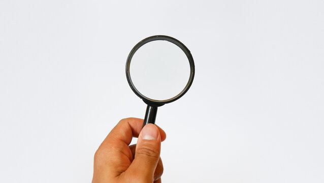 Person's hand holding a black magnifying glass isolated on white background, symbol of search, investigation, analysis, vision, and finding solutions in business or science.