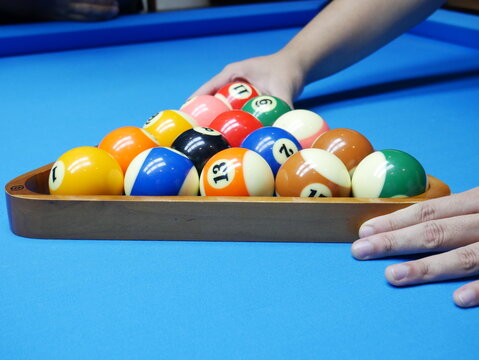 Close-up of a player racking numbered billiard balls on a vibrant blue pool table surface before a game