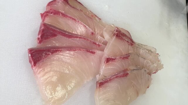 Close-up of freshly sliced amberjack kanpachi sashimi lined up on a white cutting board, Japanese izakaya, Japan