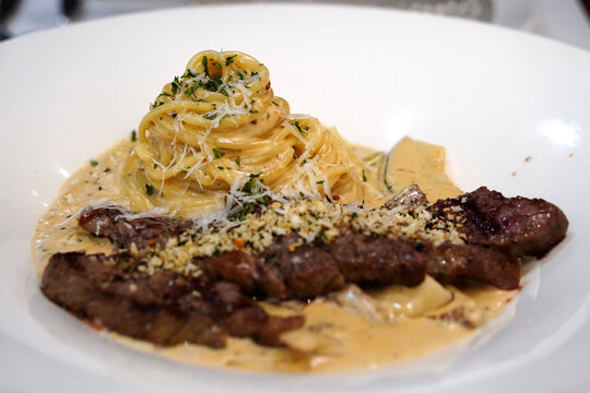 Creamy pasta topped with tender grilled beef steak slice on a white plate