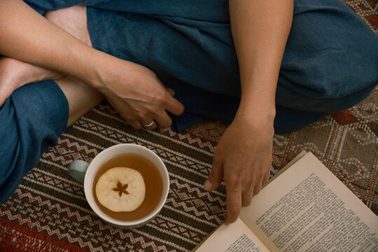 Person Sipping Hot Apple Cider While Reading Book on Rug