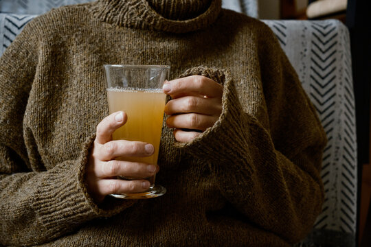 Person in Knit Sweater Holding Glass of Warm Apple Cider