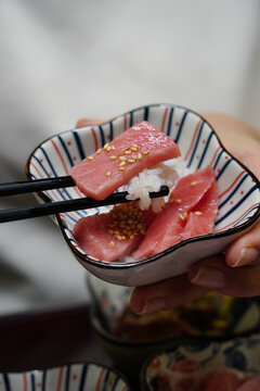 Chopsticks holding a fresh tuna sashimi slice with rice over a small bowl
