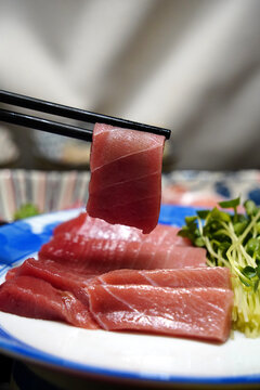 Close up view of marbled maguro tuna fish slice held by chopsticks