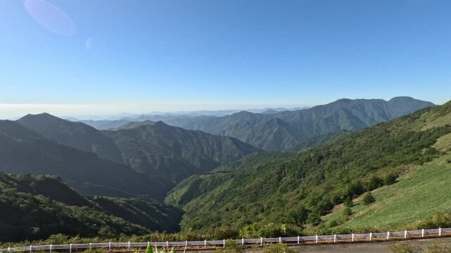 Camera tilts from a sunlit grass slope down into a deep valley