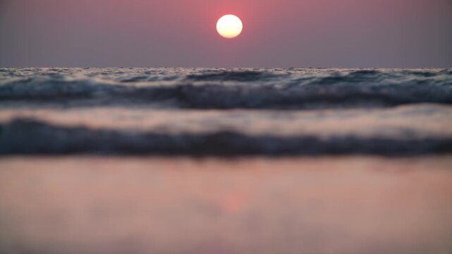 The evening sun rests above layers of sea waves, with the nearest water softly out of focus. A peaceful slow motion view of the day ending at Koh Kood, Thailand.