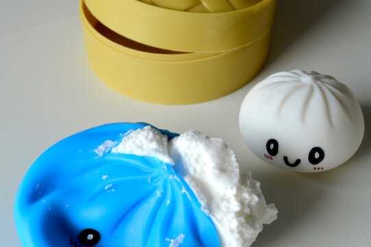 Cute kawaii squishy dumpling toys with smiling faces displayed beside a yellow bamboo steamer basket on a bright white tabletop surface
