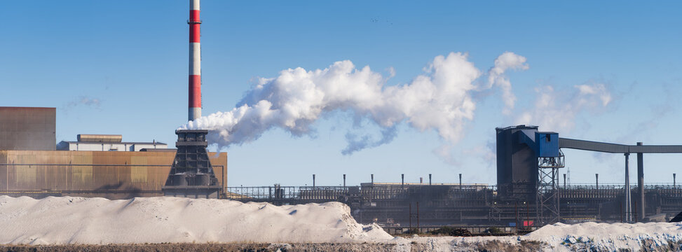 Heavy industrial steel plant with smoke emissions into the atmosphere. Wide panoramic view. Metallurgical manufacturing process and environmental air pollution.