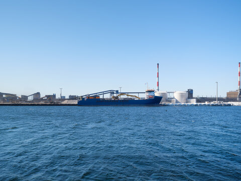 Cargo ship loading steel products at a port near a heavy industrial metallurgical plant. Industrial maritime transportation and environmental impact.