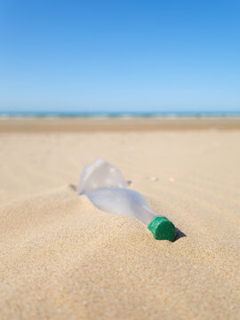 Vertical photo. Environmental waste problem on the sea coast. Plastic bottle on the beach. Plastic trash buried in the sand.