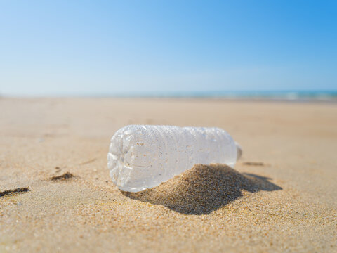 Environmental waste problem on the sea coast. Plastic bottle on the beach. Plastic trash buried in the sand.