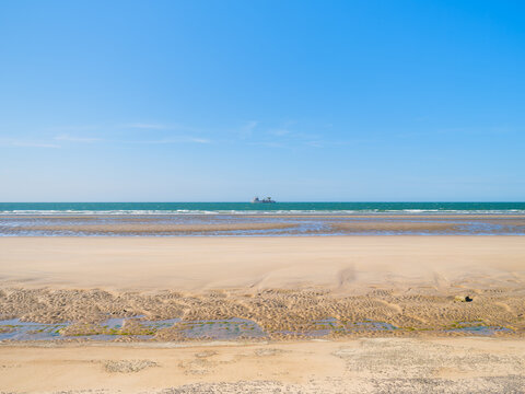 Minimalist landscape of a beach at low tide with a ship on the horizon. Summer sea travel transport during vacation.