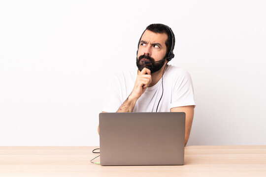 Telemarketer caucasian man working with a headset and with laptop having doubts and thinking.