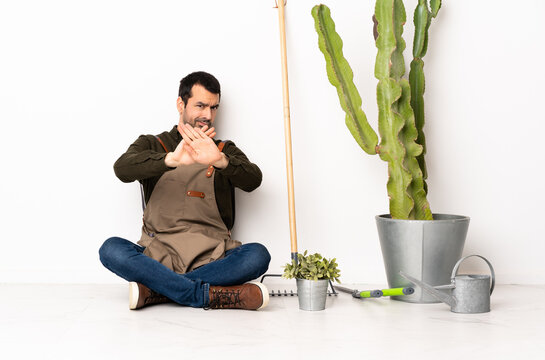 Gardener man sitting on the floor at indoors making stop gesture with her hand to stop an act