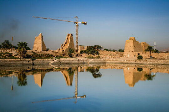 Karnak Temple pylons and construction crane reflecting in calm water in Luxor Egypt