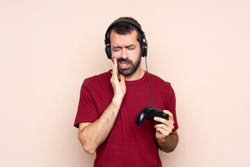 Man playing with a video game controller over isolated wall with toothache © luismolinero