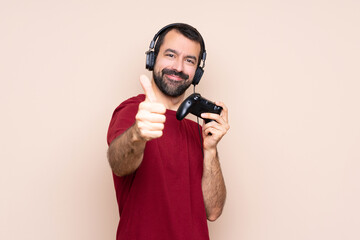 Man playing with a video game controller over isolated wall with thumbs up because something good has happened © luismolinero