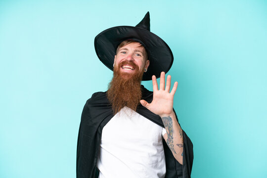 Young wizard in halloween isolated on blue background saluting with hand with happy expression