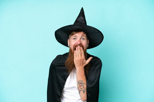 Young wizard in halloween isolated on blue background happy and smiling covering mouth with hand