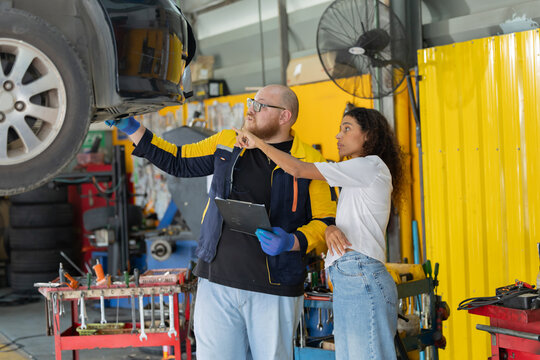 Mechanic checks car engine while customer looks on inside auto repair shop