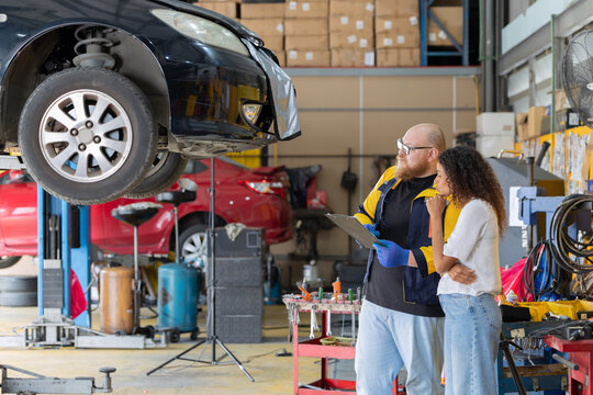 Mechanic checks car engine while customer looks on inside auto repair shop