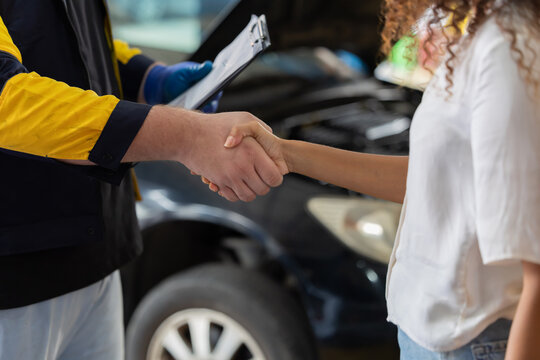 Mechanic and customer shake hands in auto repair shop during daytime in a busy garage