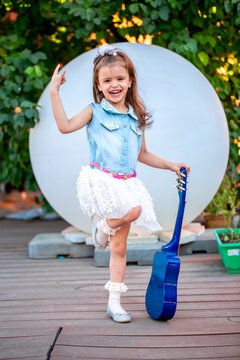 A little girl of European appearance plays the guitar on an impromptu stage, fantasizes that she is a musician. Children's games with imagination. Playing musical instruments.
