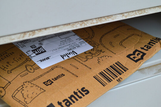 Brown cardboard delivery parcel decorated with playful hand-drawn illustrations and a white shipping label slides through a household mailbox slot