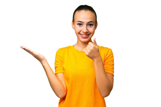 Young Arab woman over isolated background holding copyspace imaginary on the palm to insert an ad and with thumbs up