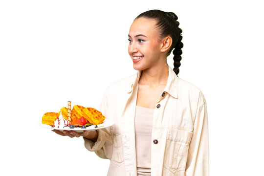 Young Arab woman holding waffles over isolated background looking side