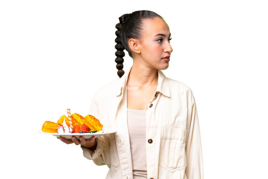 Young Arab woman holding waffles over isolated background looking to the side