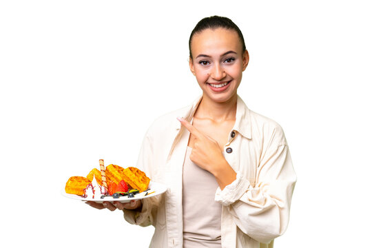 Young Arab woman holding waffles over isolated background pointing to the side to present a product