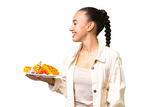 Young Arab woman holding waffles over isolated background laughing in lateral position