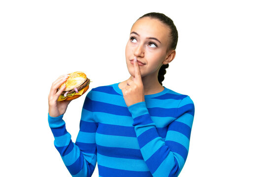 Young Arab woman holding a burger over isolated background having doubts while looking up