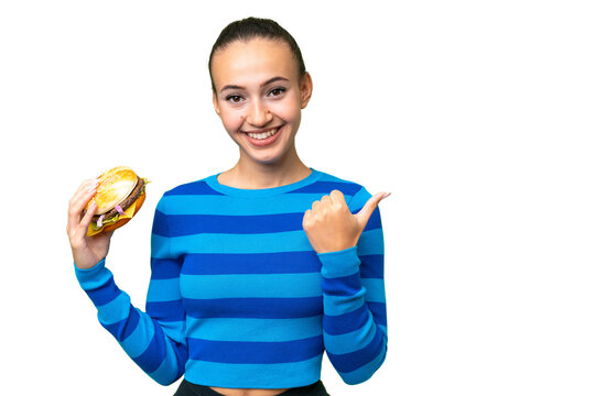 Young Arab woman holding a burger over isolated background pointing to the side to present a product