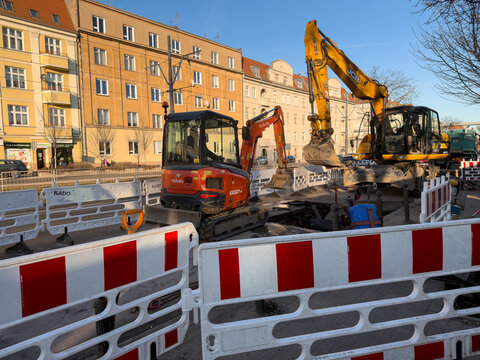 Poznan, Poland - March 3, 2026: Kubota and JCB excavators at a city street construction site with white red barriers, showing urban infrastructure repair work during daylight hours
