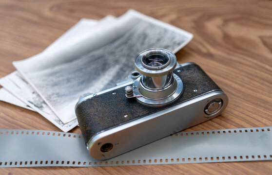 Vintage film camera with photographic negatives and film strip on wooden table. Analog photography and film imaging. Retro camera technology. Photography history and archival media.