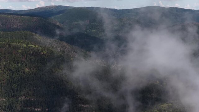Aerial of forested mountains and rolling valleys partially obscured by clouds and fog within Carson National Forest near Sipapu New Mexico