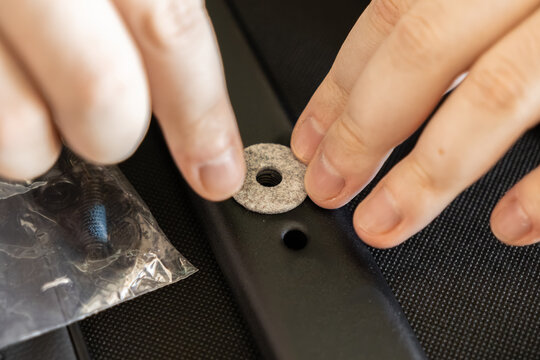 Hands placing a felt washer over a hole on a black metal furniture part, highlighting careful assembly, home improvement project, DIY repair, and furniture construction methodology
