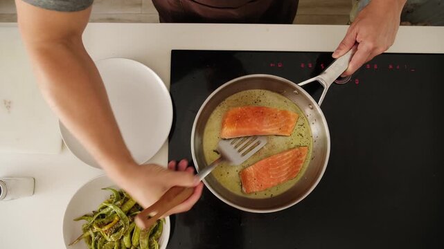 Top down view of a man pan frying salmon fillets with pepper and serving them with green beans