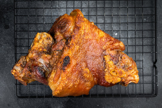Roasted Caramelized pork knuckle hock with crunchy rind texture and deep roasted color placed with thyme sprigs and mustard grains on dark slate backdrop.