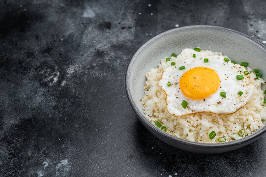 Soft rice and crisp edged fried egg in a rustic bowl photographed on dark textured background for modern culinary content.