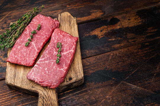 Raw marbled wagyu topside beef cut with thyme and pepper on wooden board. Premium meat for grilling roasting and cuisine.