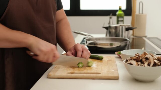 Male hands with a knife cutting fresh okra on a wooden board in a modern kitchen