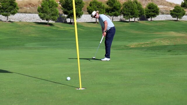 Experienced senior man practicing his golf swing and putting the ball into the hole on a beautiful green course during a sunny day, showcasing a leisurely and recreational sporting activity