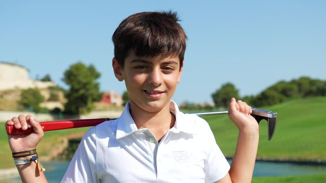 Portrait of a smiling young male golfer holding a putter on his shoulders while standing on a beautiful green course, with a lake and clear blue sky in the background on a sunny day