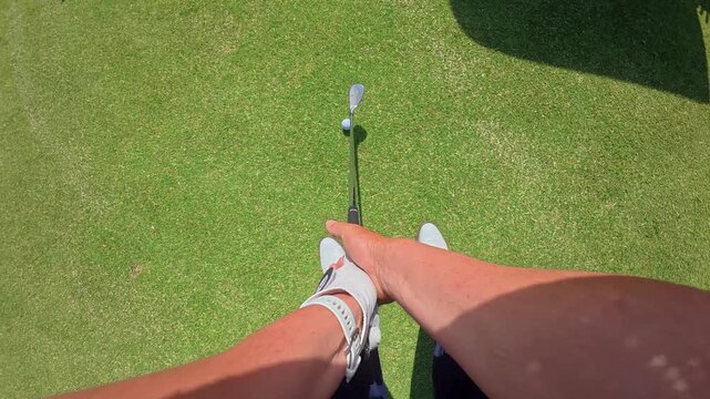 Point of view shot of a male golfer holding a club and preparing for a swing on a beautiful green fairway under a clear blue sky, demonstrating proper grip and stance during a game