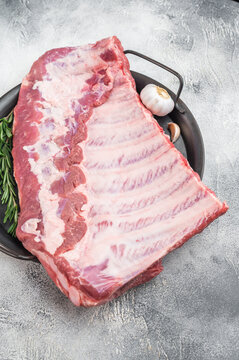 Fresh uncooked pork spareribs slab with bone styled with herbs overhead barbecue preparation on textured light background