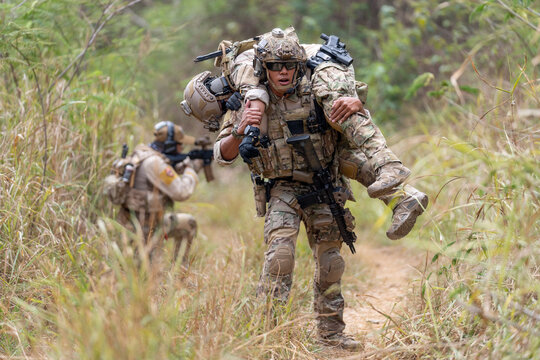 Soldier carrying injured comrade through tall grassy terrain with focused determination
