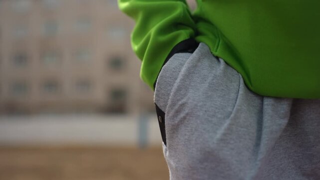 fingers modifying sweatshirt pocket edge detail, thumbnails and fingers adjusting trousers pocket in outdoor setting, closeup view of fingers altering edge of sweatshirt pocket outdoors in courtyard